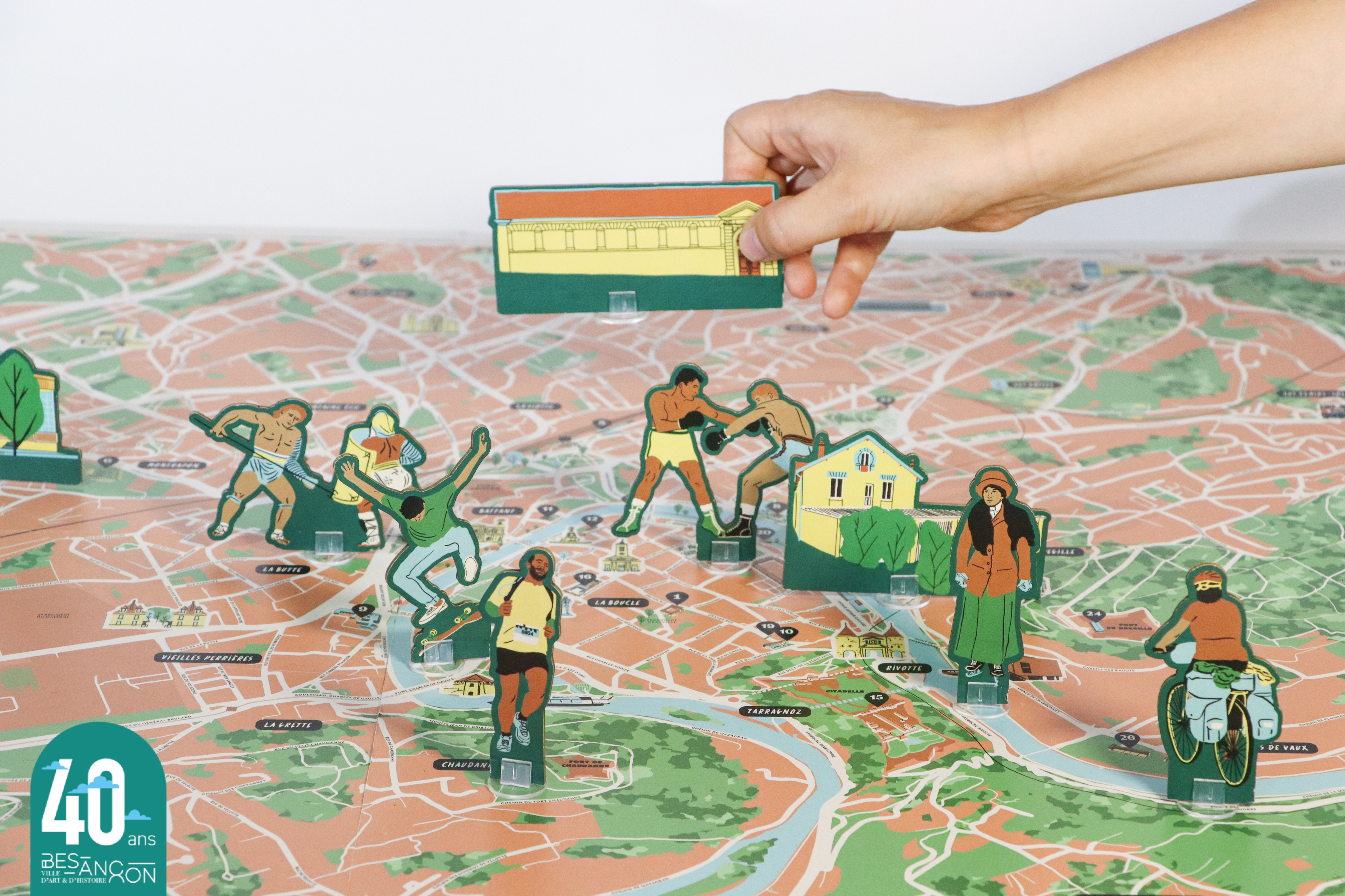 photographie d'une main déposant un pion sur un plateau de jeu représentant la ville de Besançon